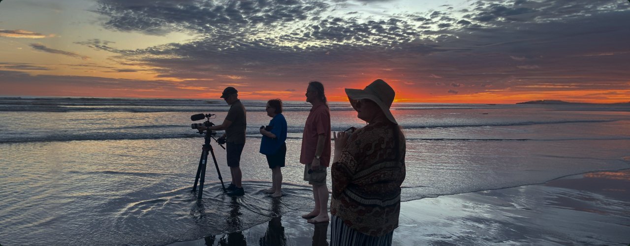 Authors filming on a beach at sunset